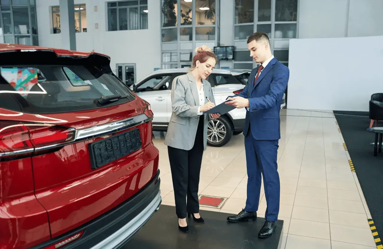 Kobieta podpisuje dokumenty przy nowej, czerwonej Toyocie. To jej pierwszy przegląd gwarancyjny.