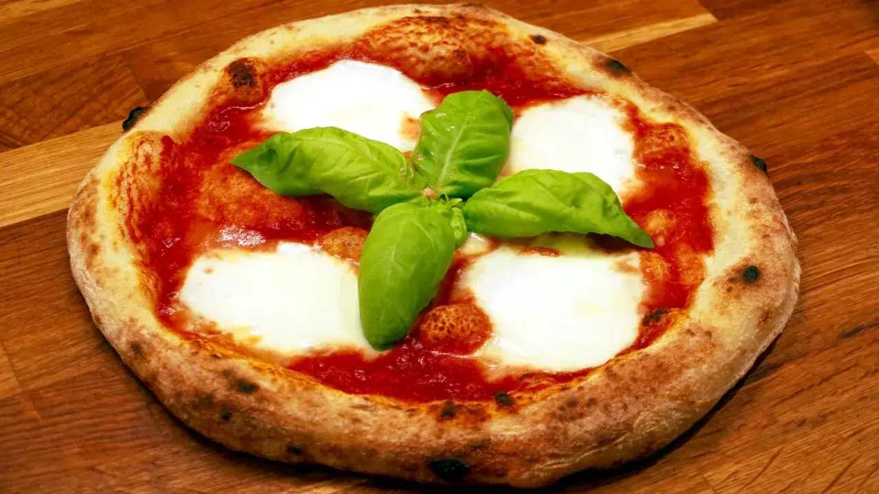 En napolitansk pizzadeg snabb, toppad med tomatsås, mozzarella och färsk basilika, ligger på en träyta.