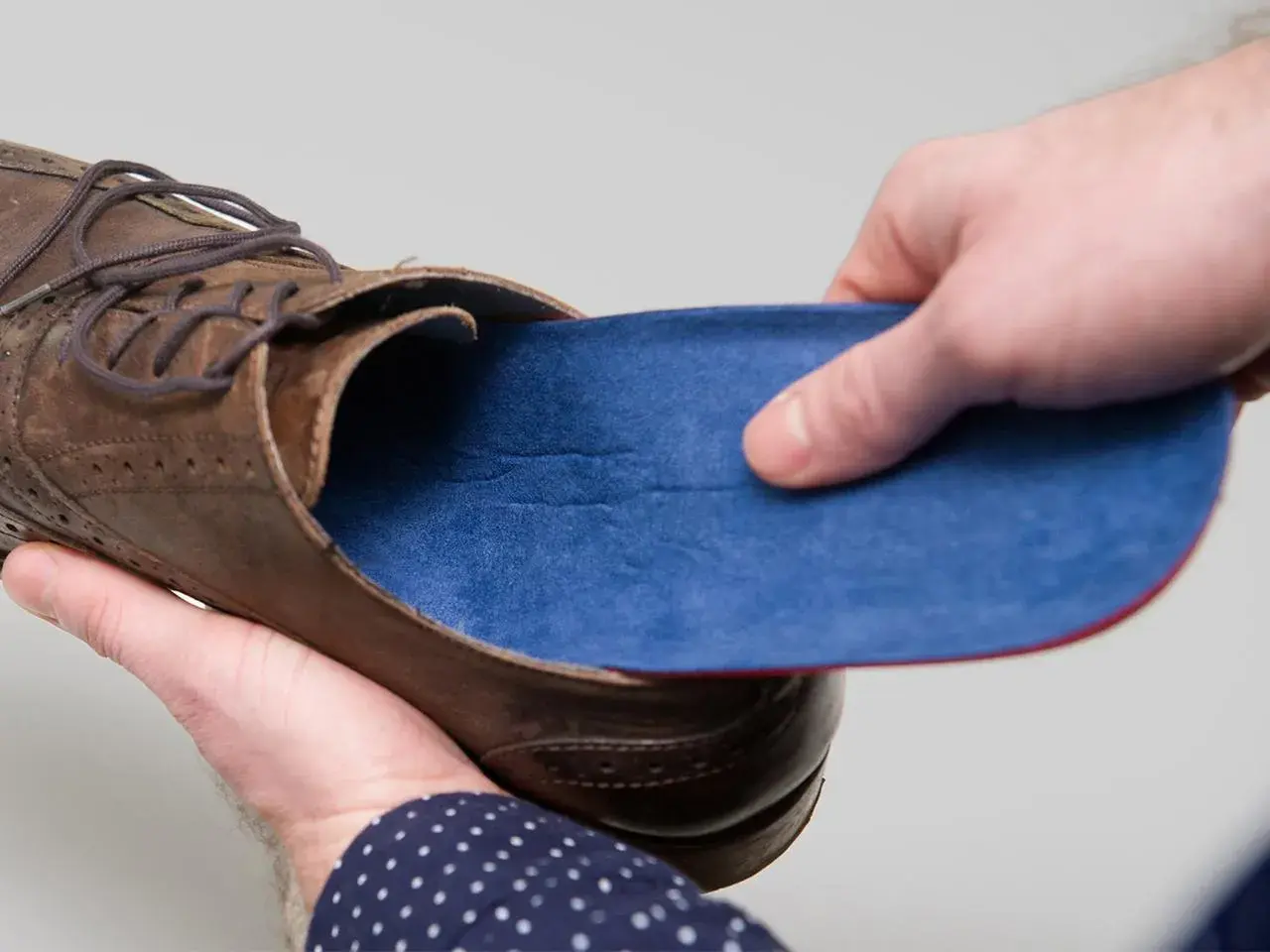 Braune Lederschuhe mit blauen Innenschuhen. Eine Hand hält die Einlage, die andere den Schuh.