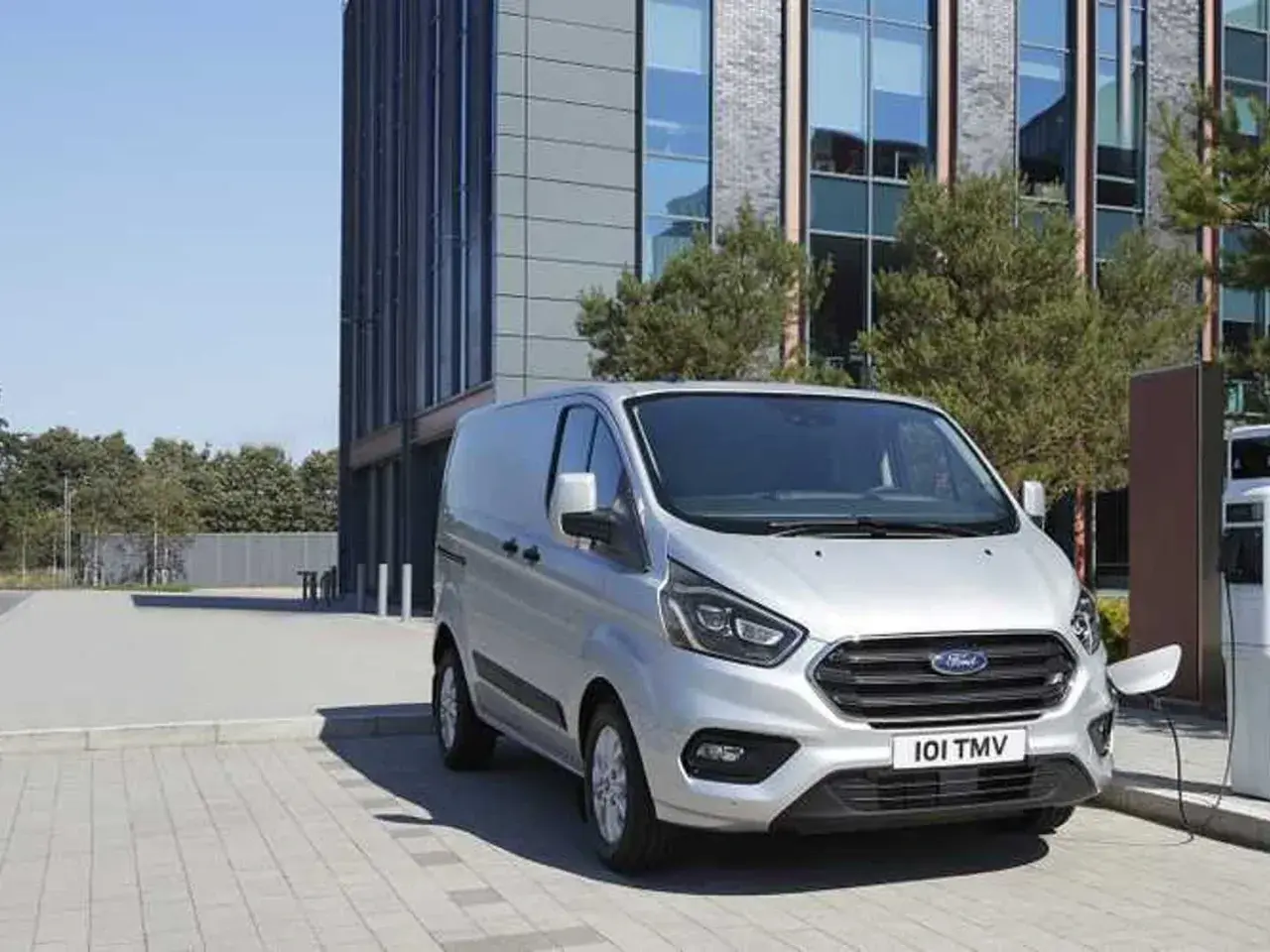 Furgoneta Ford Transit plateada cargando, con un edificio moderno al fondo. La presión de los neumáticos es clave para su eficiencia.