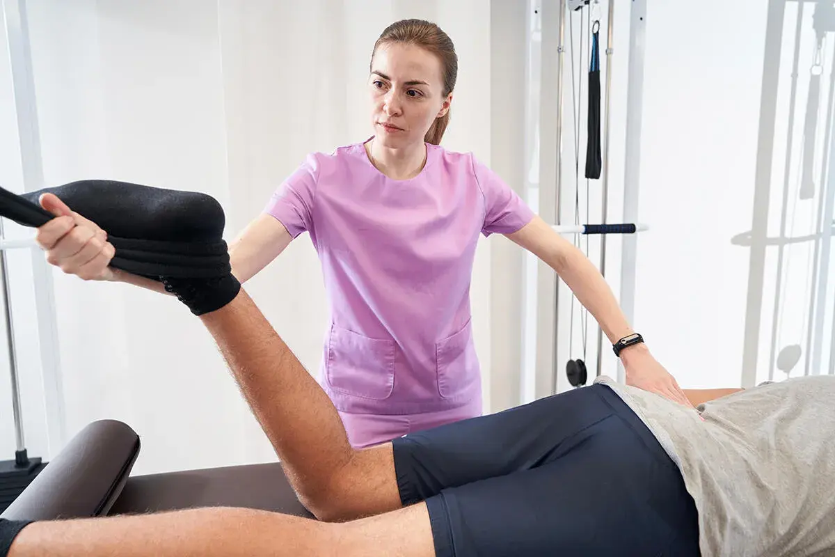Fizjoterapeutka wykonuje test Mennella, pomagając pacjentowi w rehabilitacji kończyny dolnej.