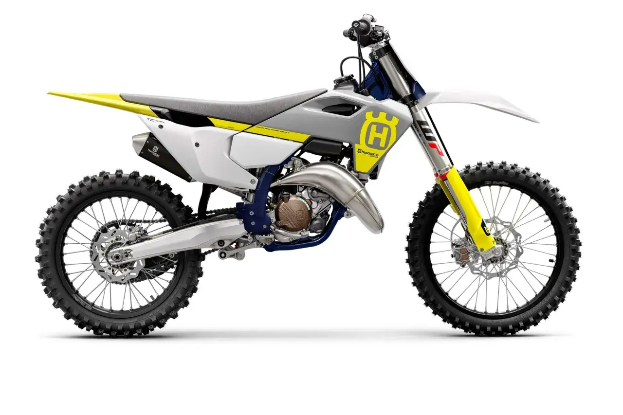 Motocykl crossowy Husqvarna TC125 w kolorze białym z żółtymi i niebieskimi akcentami, gotowy do wyścigów.
