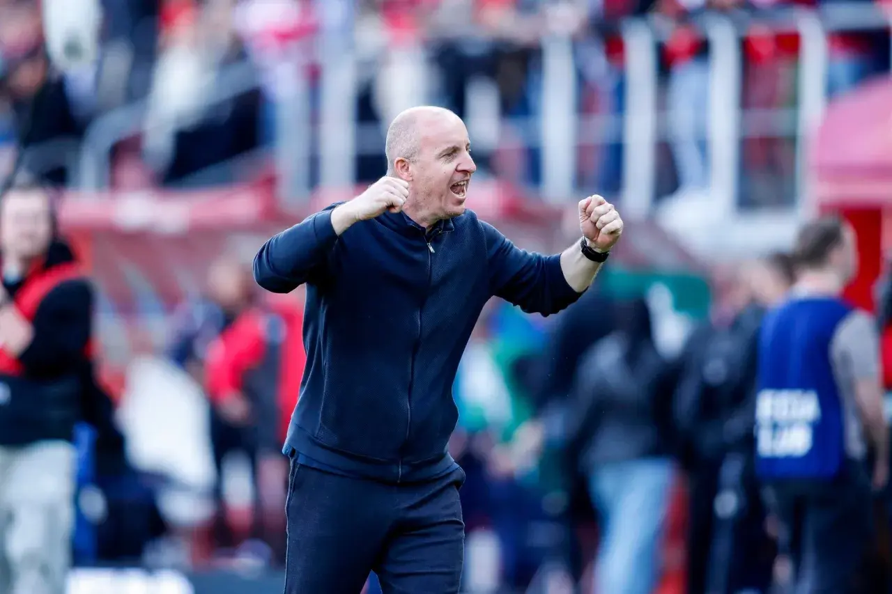 Nowy trener Widzewa, z zaciśniętymi pięściami, krzyczy z radości na tle trybun.