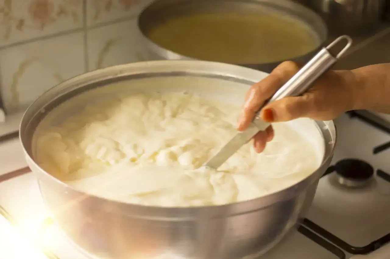 Mano che mescola un pentolone pieno di cremoso yogurt da bere fatto in casa, pronto per essere gustato.