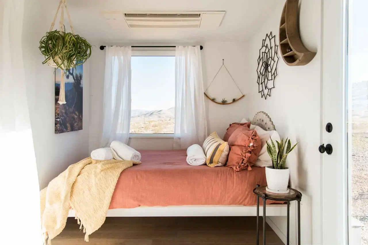 Cozy small bedroom layout with a bed, window view, hanging plants, and desert-inspired decor.