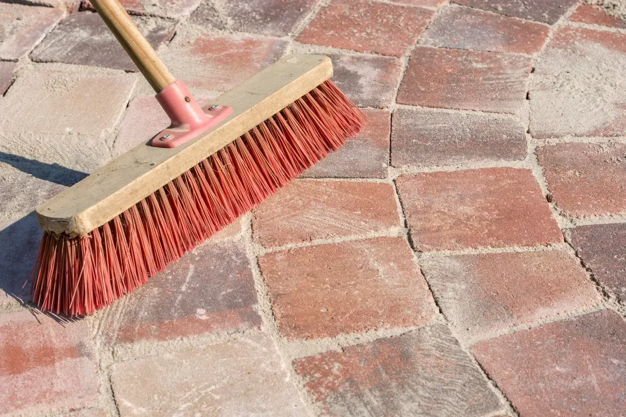 Una scopa con setole rosse su sanpietrini rossi e sabbia. Un modo semplice per capire come pulire i sanpietrini.