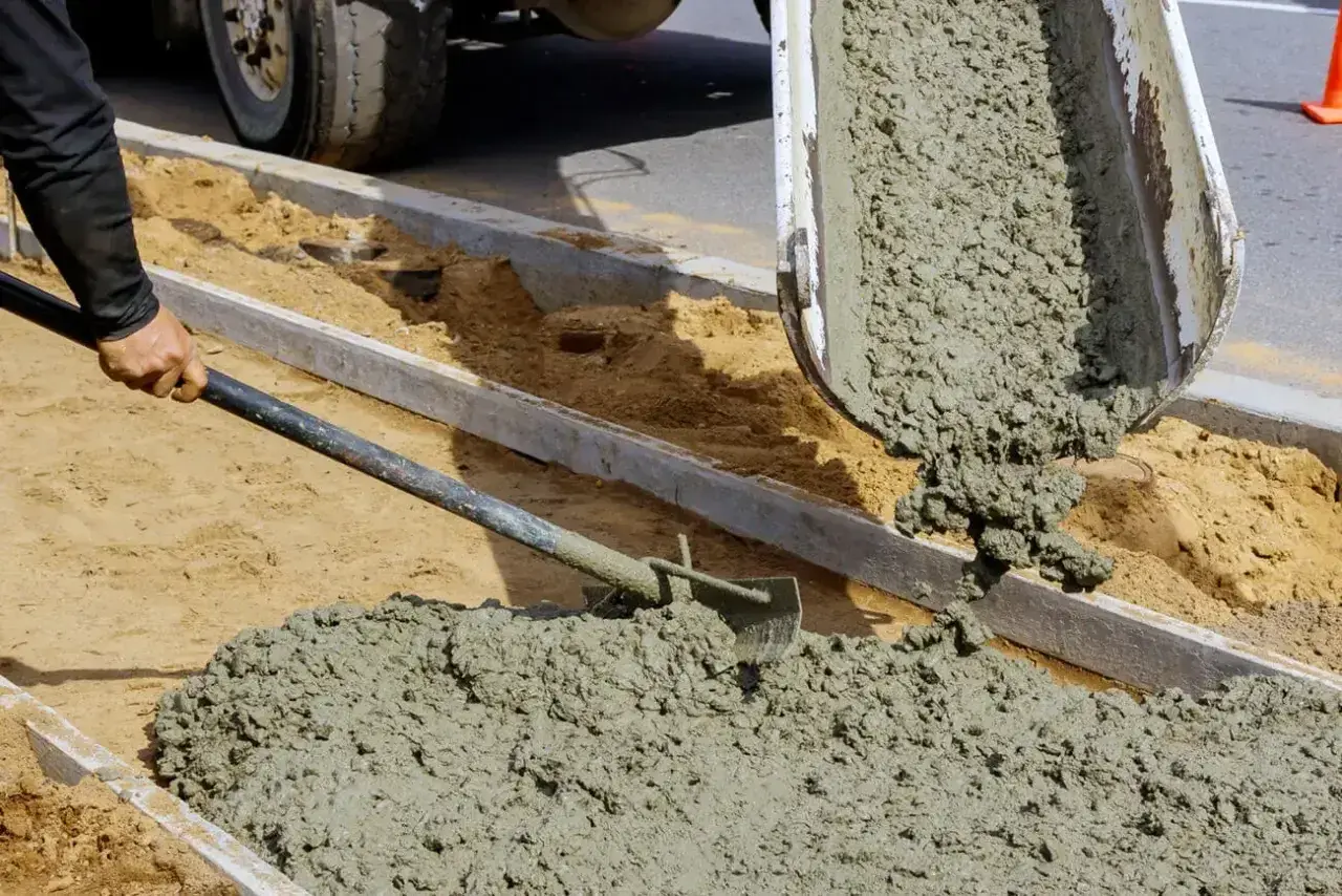 Robotnik rozprowadza łopatą świeży cement z wodą bez piasku, wylewany z betoniarki na budowie.