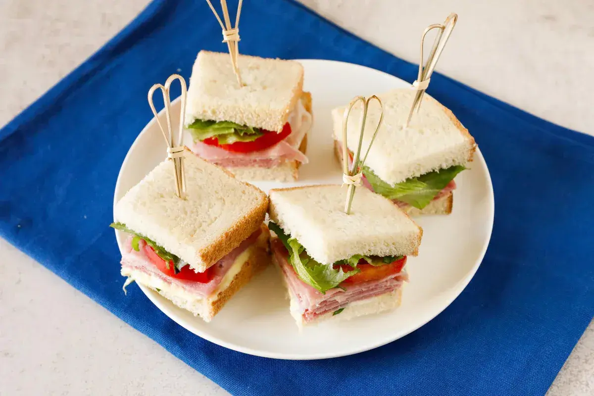 Quattro tramezzini quadrati con prosciutto, lattuga e pomodoro, perfetti per idee gusti tramezzini veloci e sfiziosi.