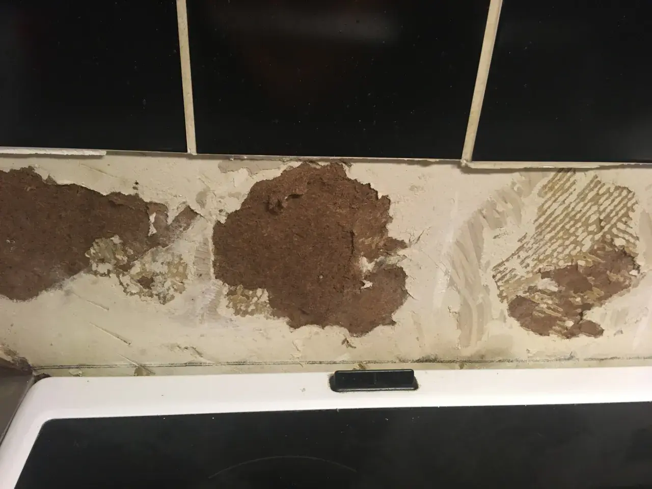 Skadad vägg där kakel lossnat och blottar masonit. En renovering behövs.