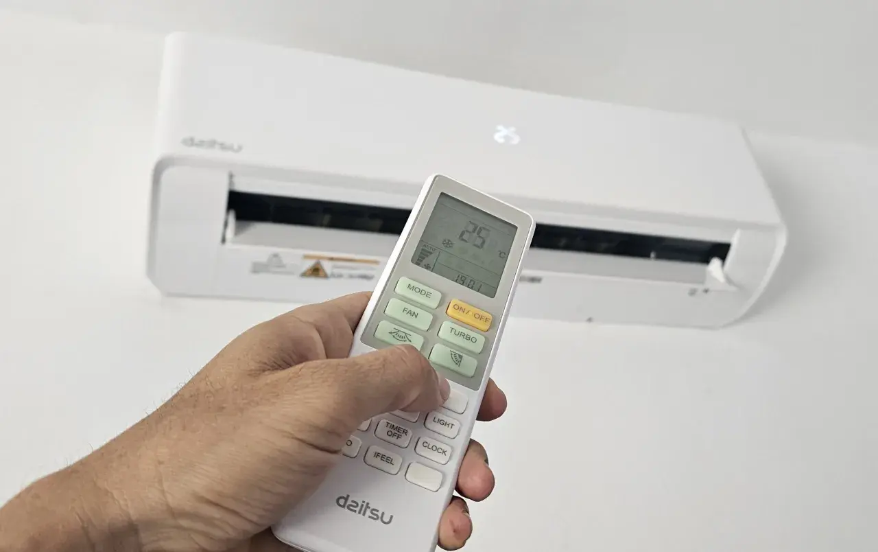 Mano ajustando el control remoto de un aire acondicionado Daitsu. Para poner el aire acondicionado en invierno, selecciona el modo "Calor" o "Heat" en el control.