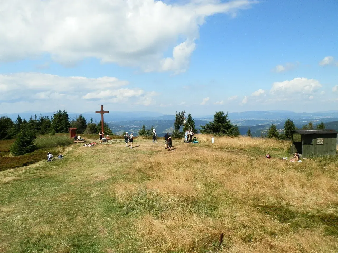 Wielka racza szlaki to widok na szczyt z krzyżem i ludźmi odpoczywającymi na trawie.