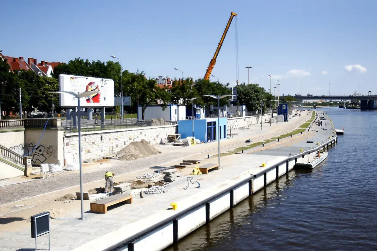 Trwa rewitalizacja Bulwaru Piastowskiego w Szczecinie. Widoczny plac budowy, dźwig i pracownicy nad Odrą.