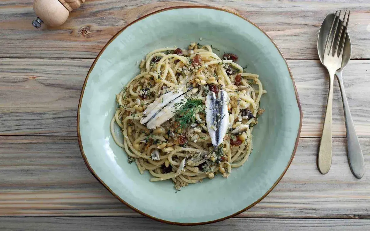 Assiette de pâtes au poisson italienne, garnie d'anchois, de pignons de pin et de raisins secs.