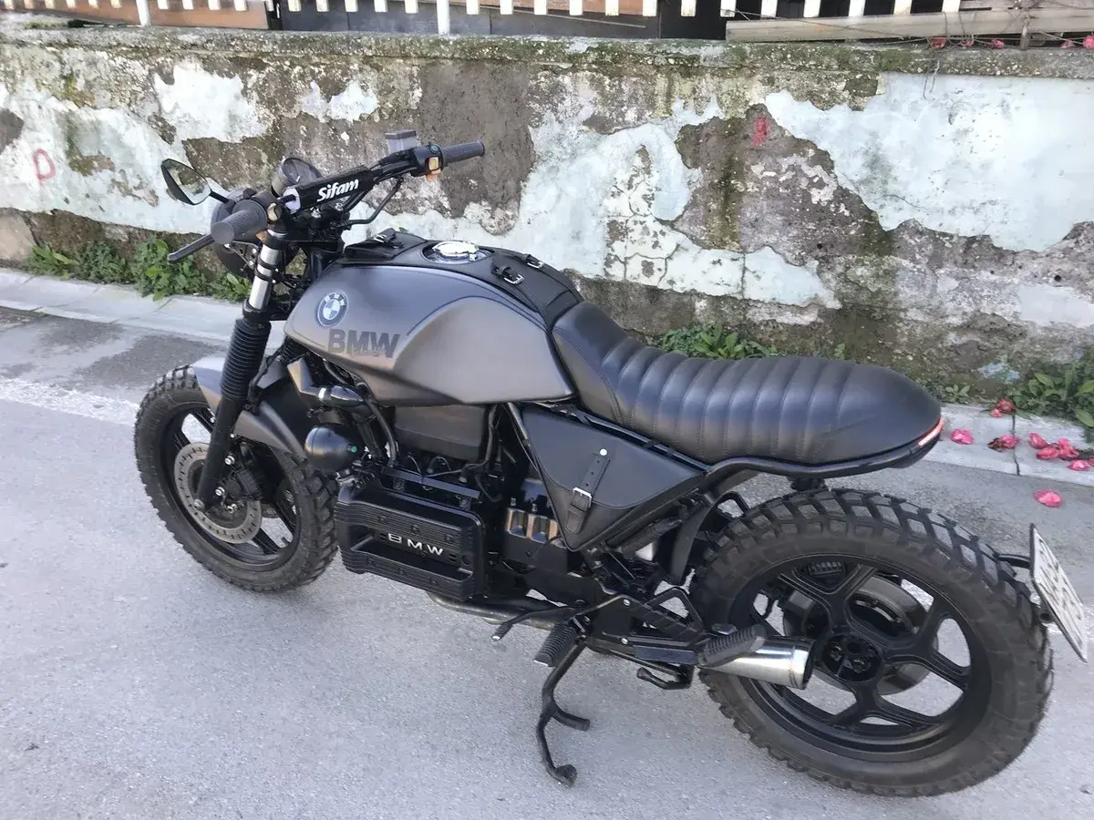 Moto BMW customizzata in stile cafe racer, con serbatoio grigio opaco, sella nera e borse moto laterali in pelle.