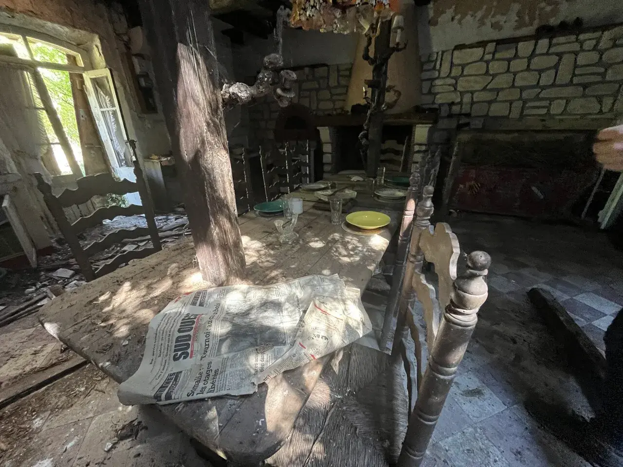 Table dressée dans une maison abandonnée, vestige d'un urbex à Bordeaux. Lumière filtrant par la fenêtre, poussière sur les assiettes.