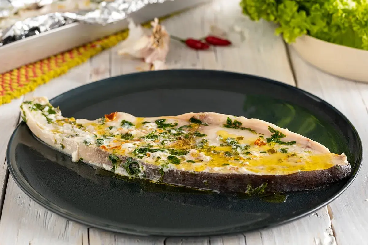Un succulento pesce spada al forno, condito con erbe aromatiche e olio d'oliva, servito su un piatto scuro.