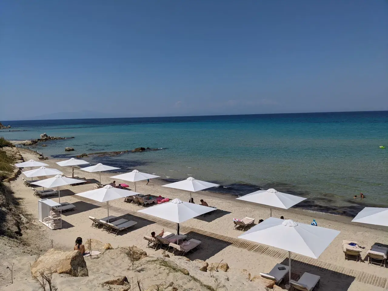 Traumhafter Karibik-Strand auf Chalkidiki mit weißen Sonnenschirmen und Liegen am türkisfarbenen Meer.