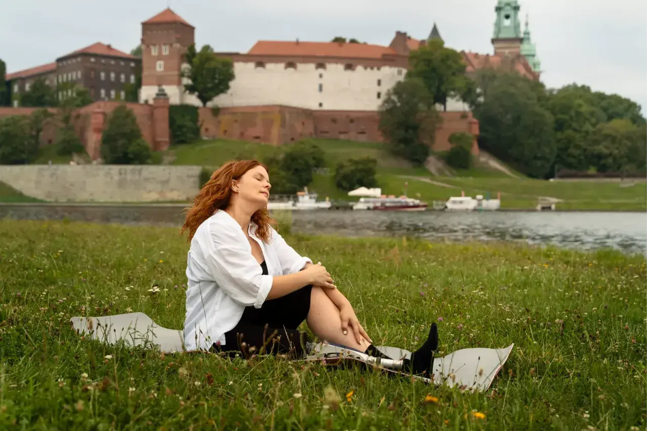 Kobieta z rudymi włosami odpoczywa na trawie z widokiem na Wawel. Idealne miejsce na jednodniowe wycieczki z Krakowa.