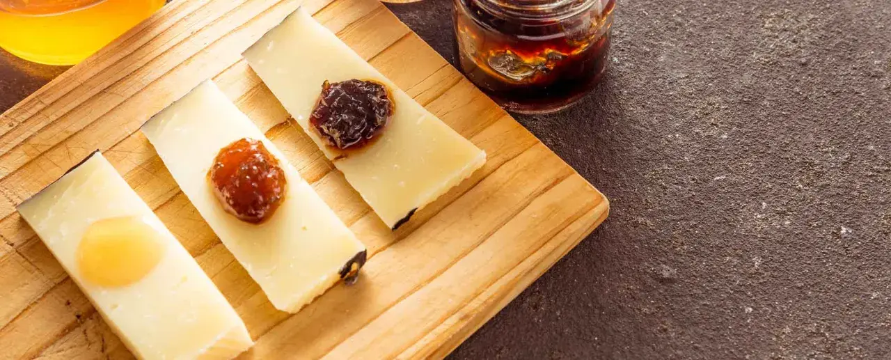 Fette di formaggio con miele e marmellata su tagliere. Perfetto per capire quanto può stare il formaggio fuori dal frigo.