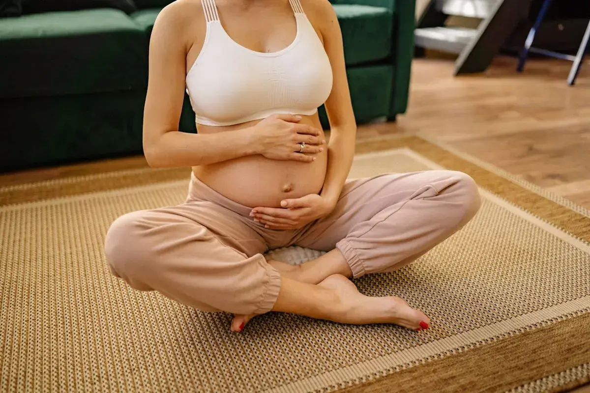 Donna incinta seduta a gambe incrociate sul tappeto, mani sull'addome. Si percepiscono i movimenti del feto a diverse altezze.