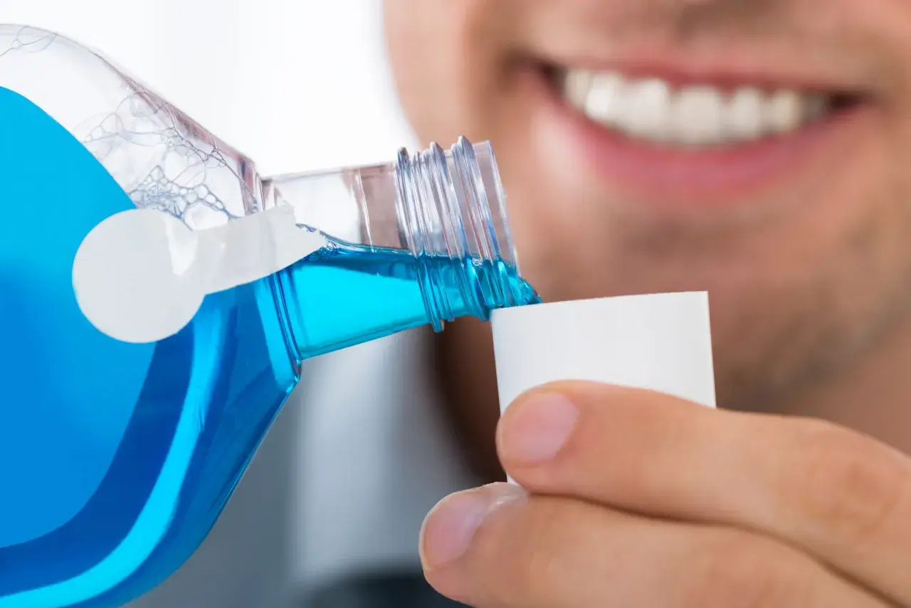 Un uomo versa colluttorio blu in un tappo, un gesto di cura dopo l'estrazione di un dente.