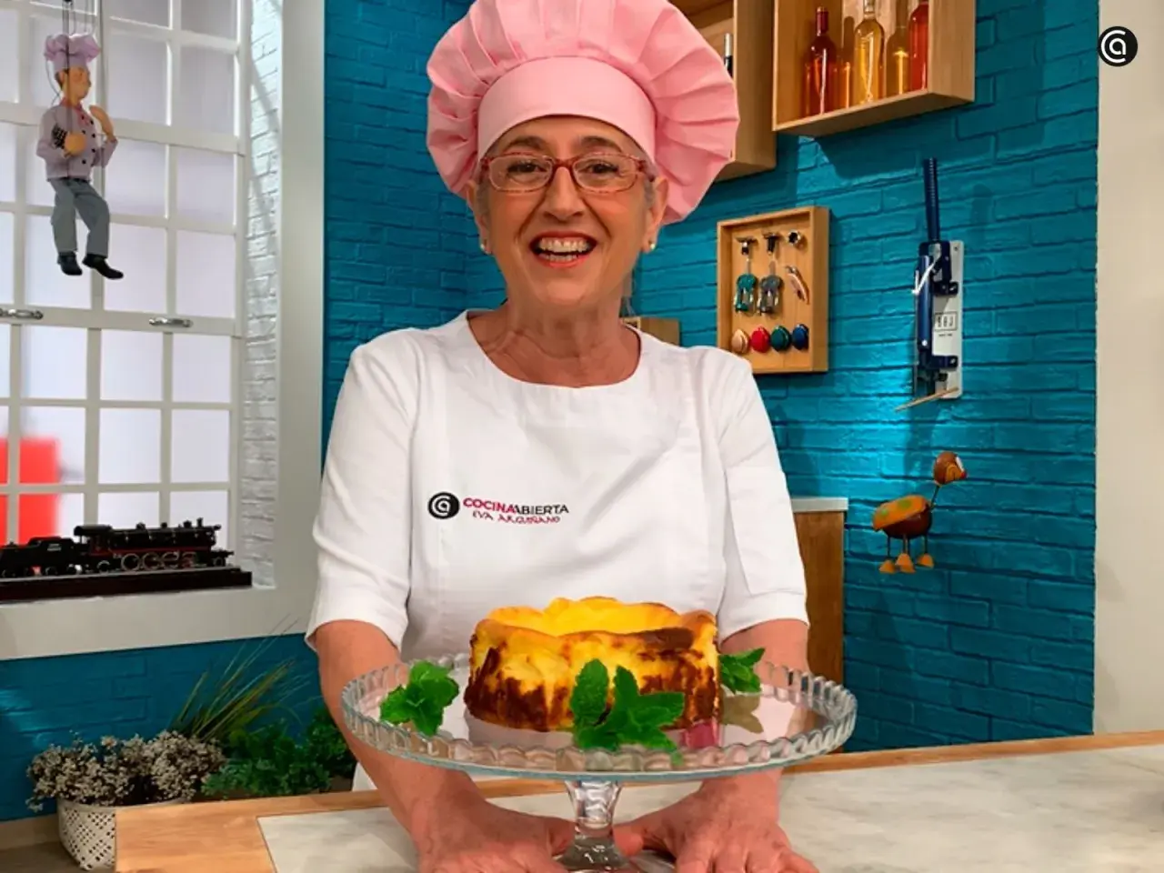 Eva Arguiñano sonríe mostrando una deliciosa tarta de queso casera, decorada con menta fresca.