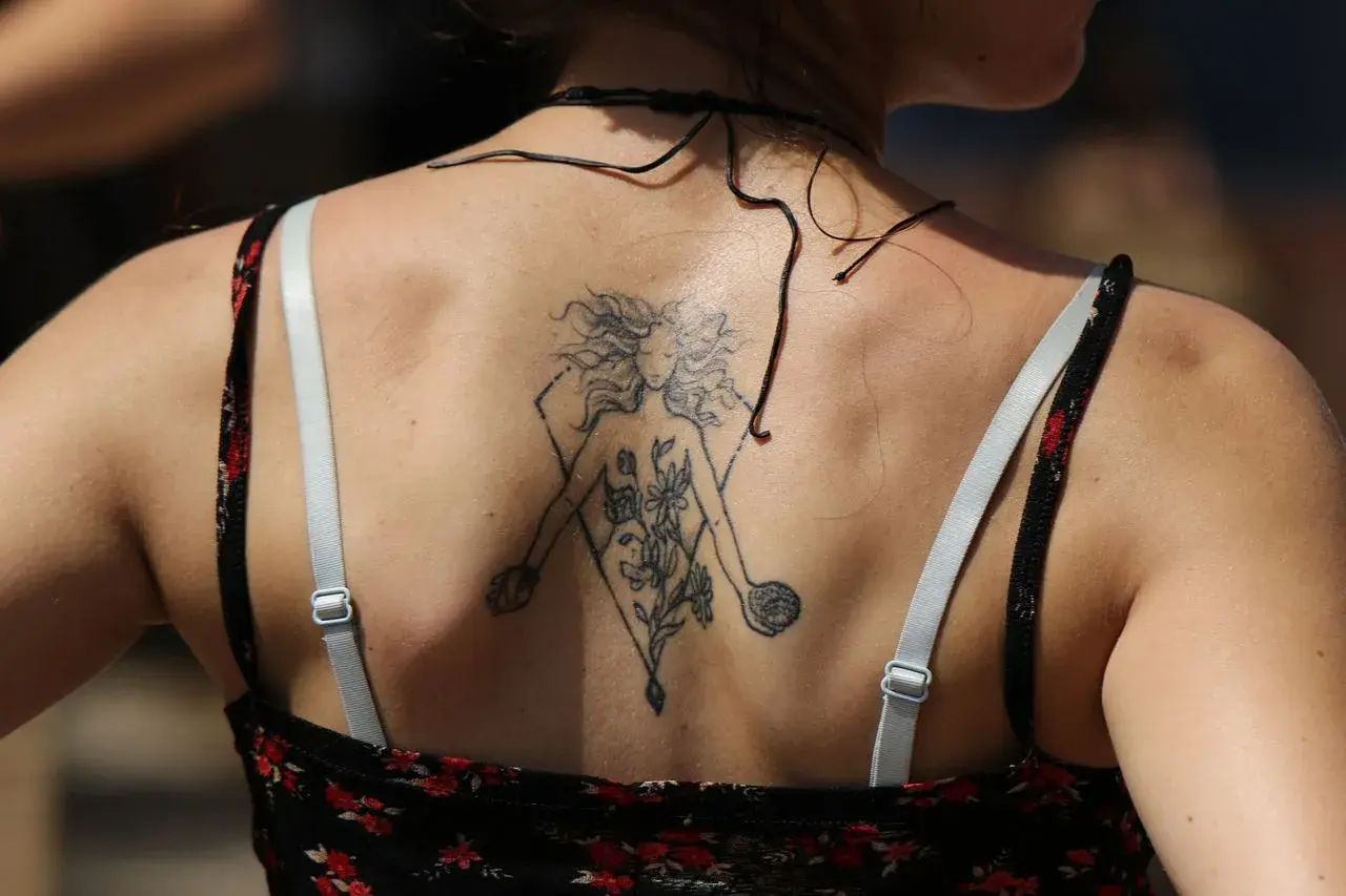 Tatuaz znak zodiaku na plecach kobiety, przedstawiający postać z kwiatami w geometrycznej ramie.