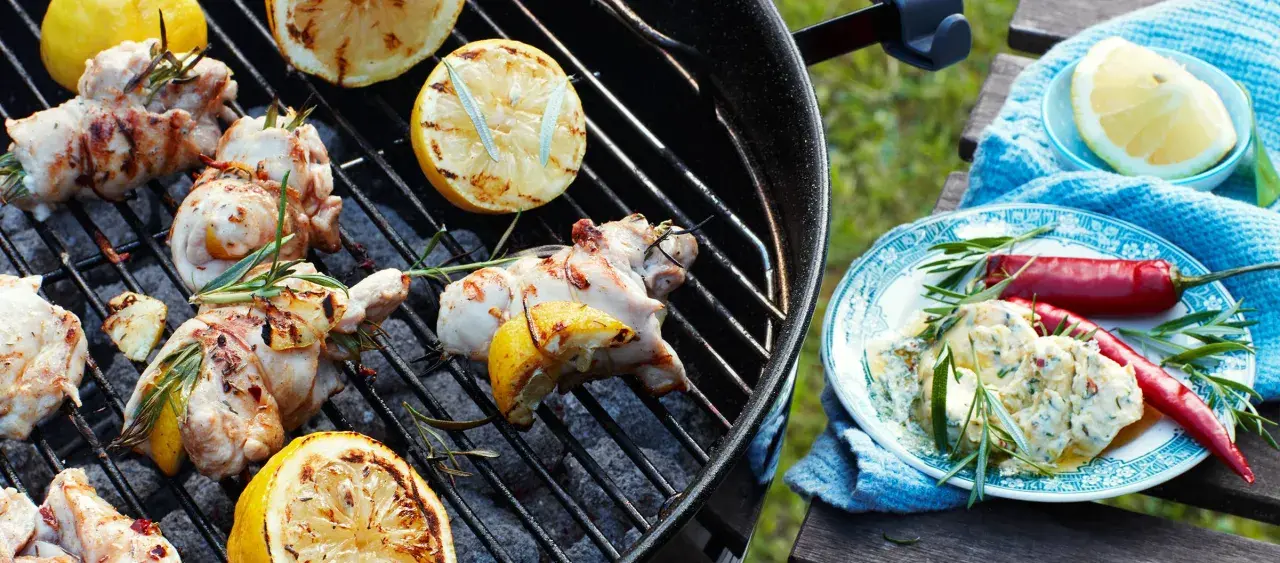 Grillad kyckling med citron och rosmarin på grillen. En tallrik med kyckling, chilifrukter och örtsås står bredvid.