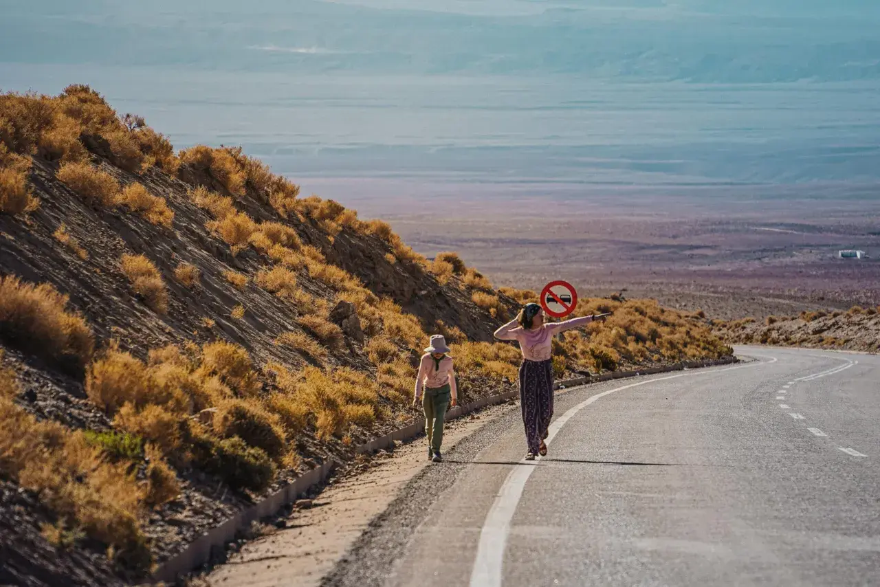 Dwie dziewczynki w kolorowych ubraniach idą pustynią Atacama. Jedna z nich trzyma znak zakazu ruchu.