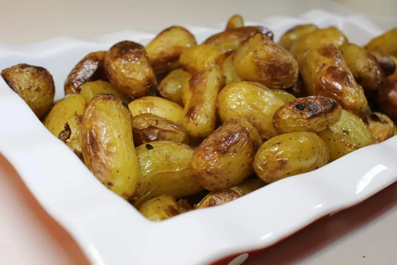 Un plat blanc rempli de pommes de terre nouvelles rôties, dorées et appétissantes.