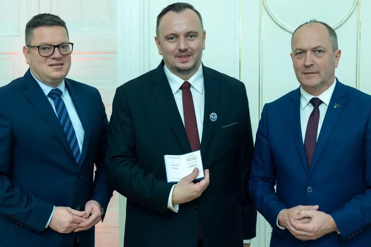 Trzech mężczyzn w garniturach. Środkowy, zasłużony dla kolejnictwa, trzyma certyfikat.