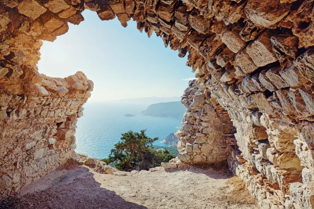 Blick durch eine Felsenruine auf das azurblaue Meer. Ein absolutes Rhodos Must See für Geschichts- und Naturliebhaber.