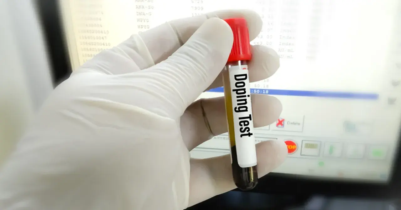 Rękawiczka trzyma probówkę z napisem "Doping Test". Wyniki badań na ekranie sugerują, czy testosteron jest legalny w sporcie.