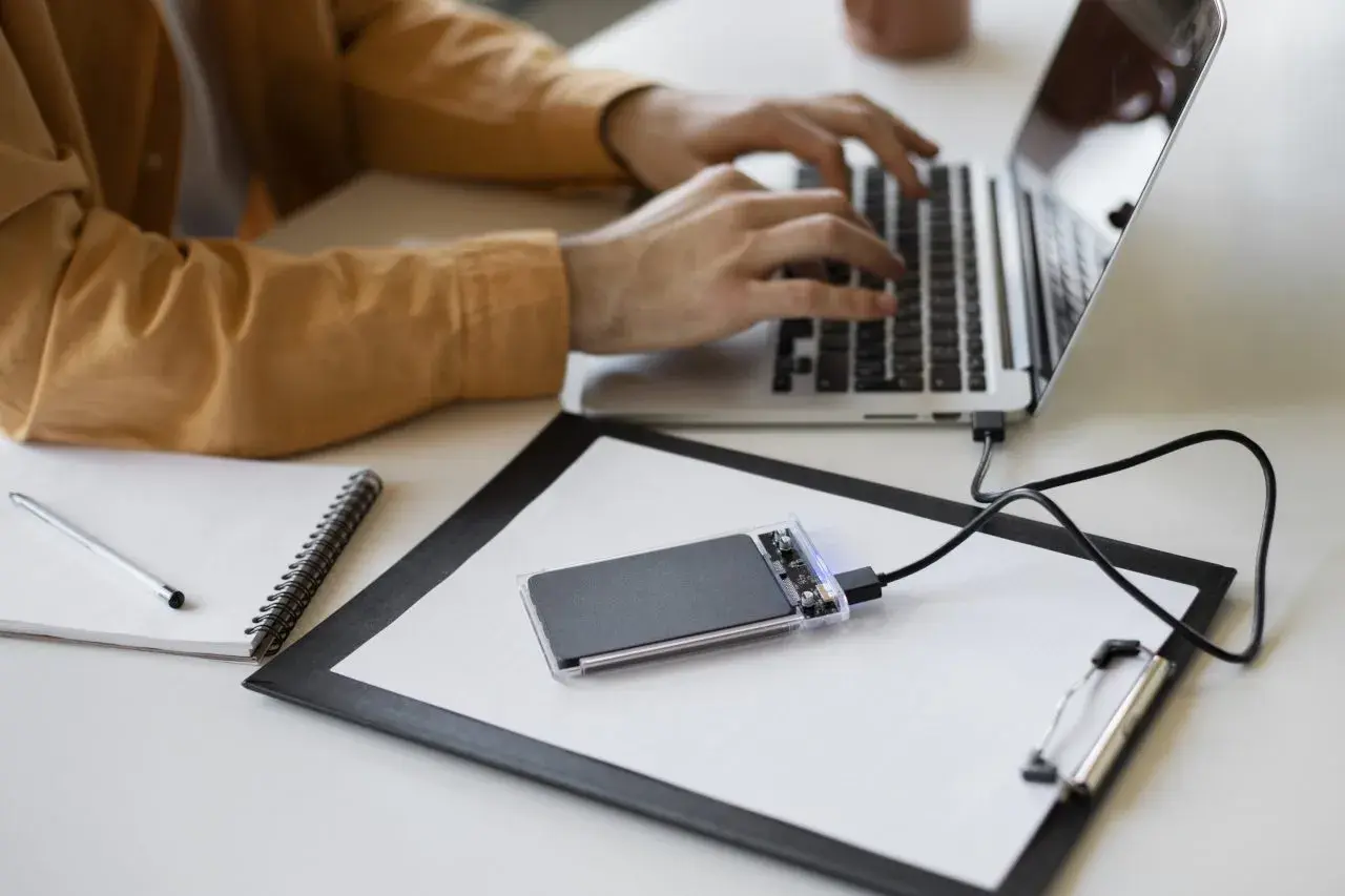 Un homme tape sur son ordinateur portable, un disque SSD externe est branché.
