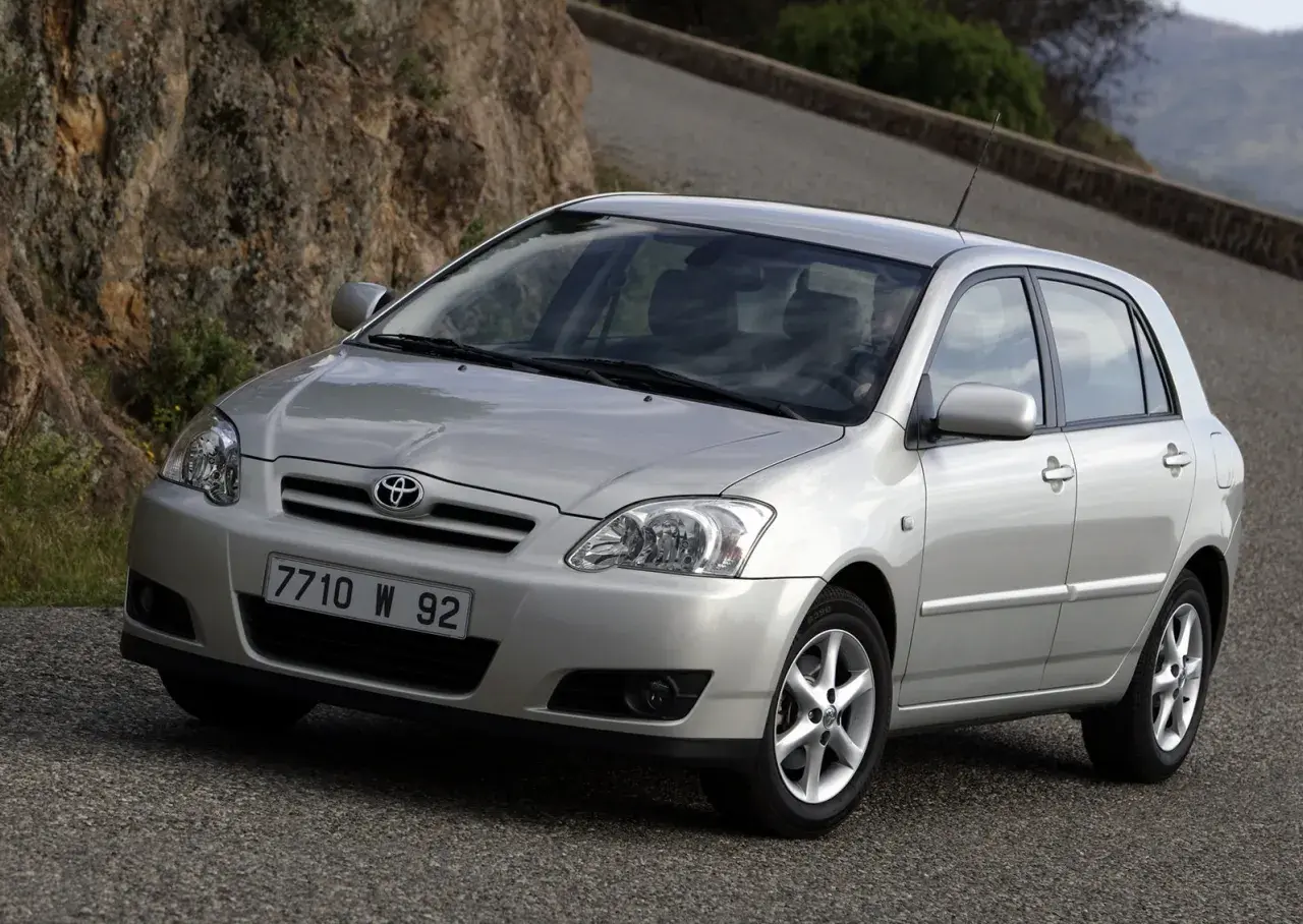 Srebrna Toyota Corolla E12 hatchback na krętej drodze wśród skał i zieleni.