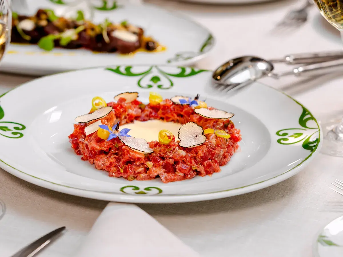 Delicioso tartar de atún fresco, adornado con láminas de trufa negra, flores comestibles y un toque de limón.