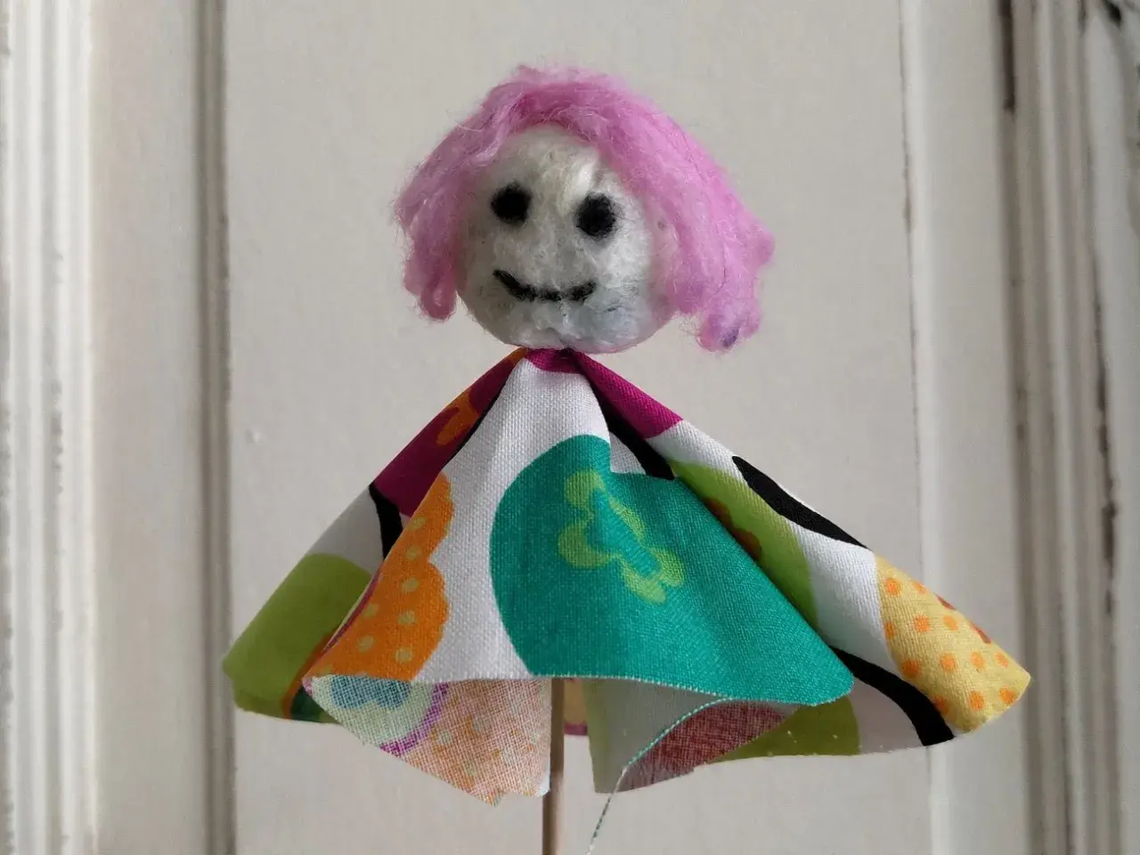 Eine selbstgemachte Puppe mit pinker Wolle als Haar und buntem Stoffkleid. Perfekt zum Filzen mit Kindern.