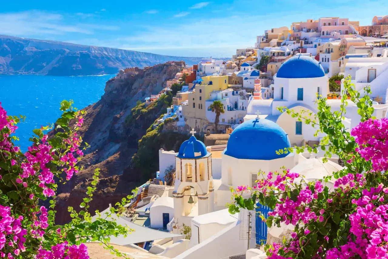 Vue panoramique de Oia, Santorin, l'une des plus belles îles grecques, avec ses dômes bleus iconiques et ses bougainvilliers roses éclatants.