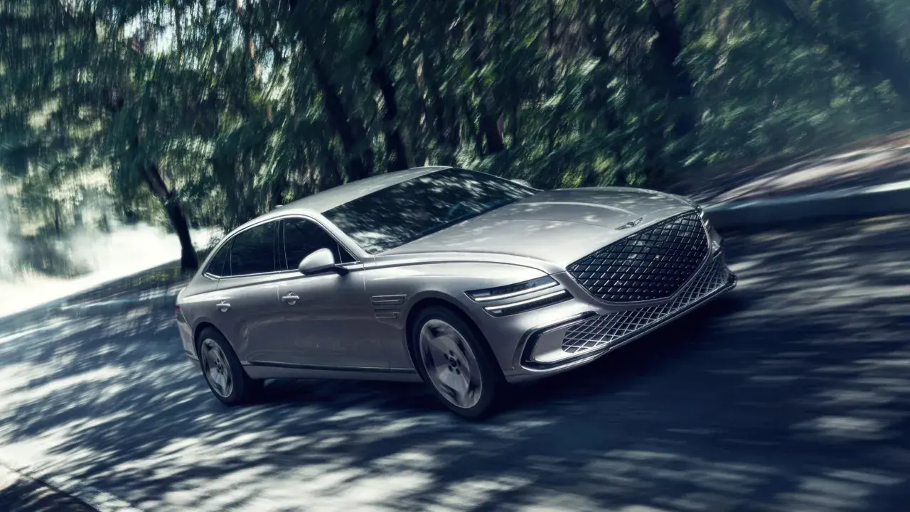 Silver Genesis G80 Sverige glider genom en skogsväg, skuggor dansar över bilen.