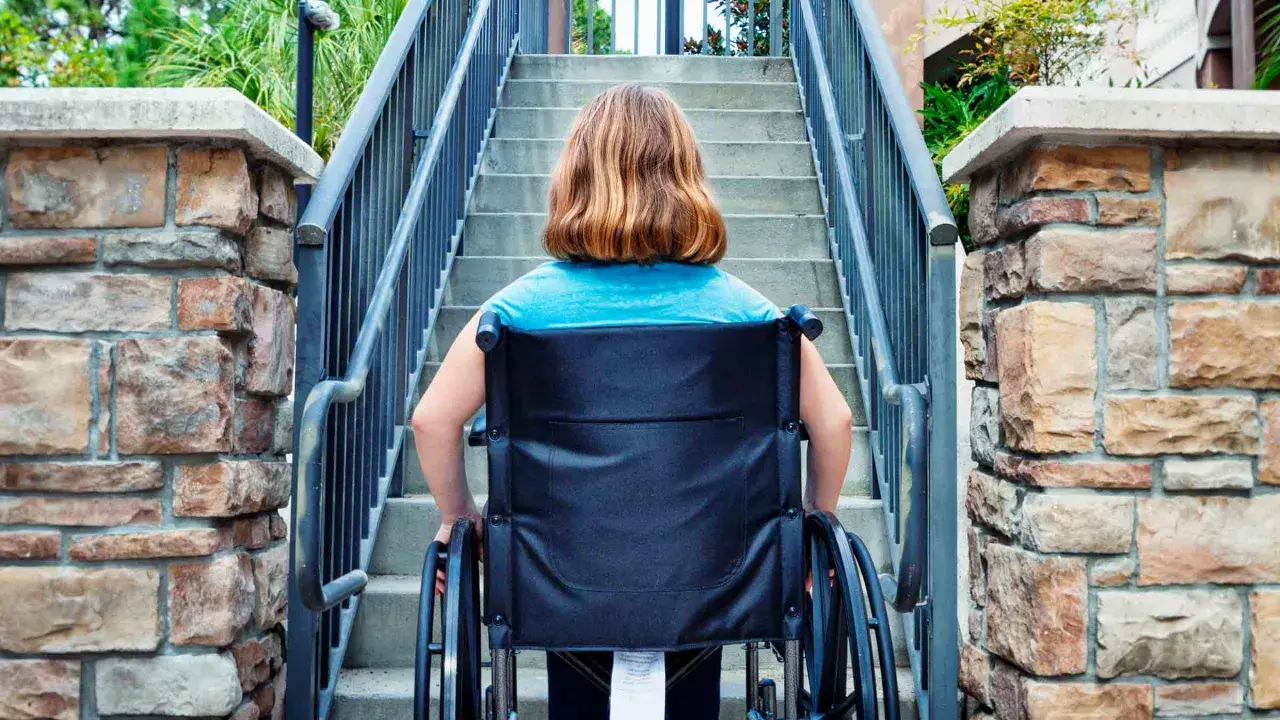 Ragazza in carrozzina affronta una scalinata, un aiuto per l'accessibilità come previsto dalla legge 104.