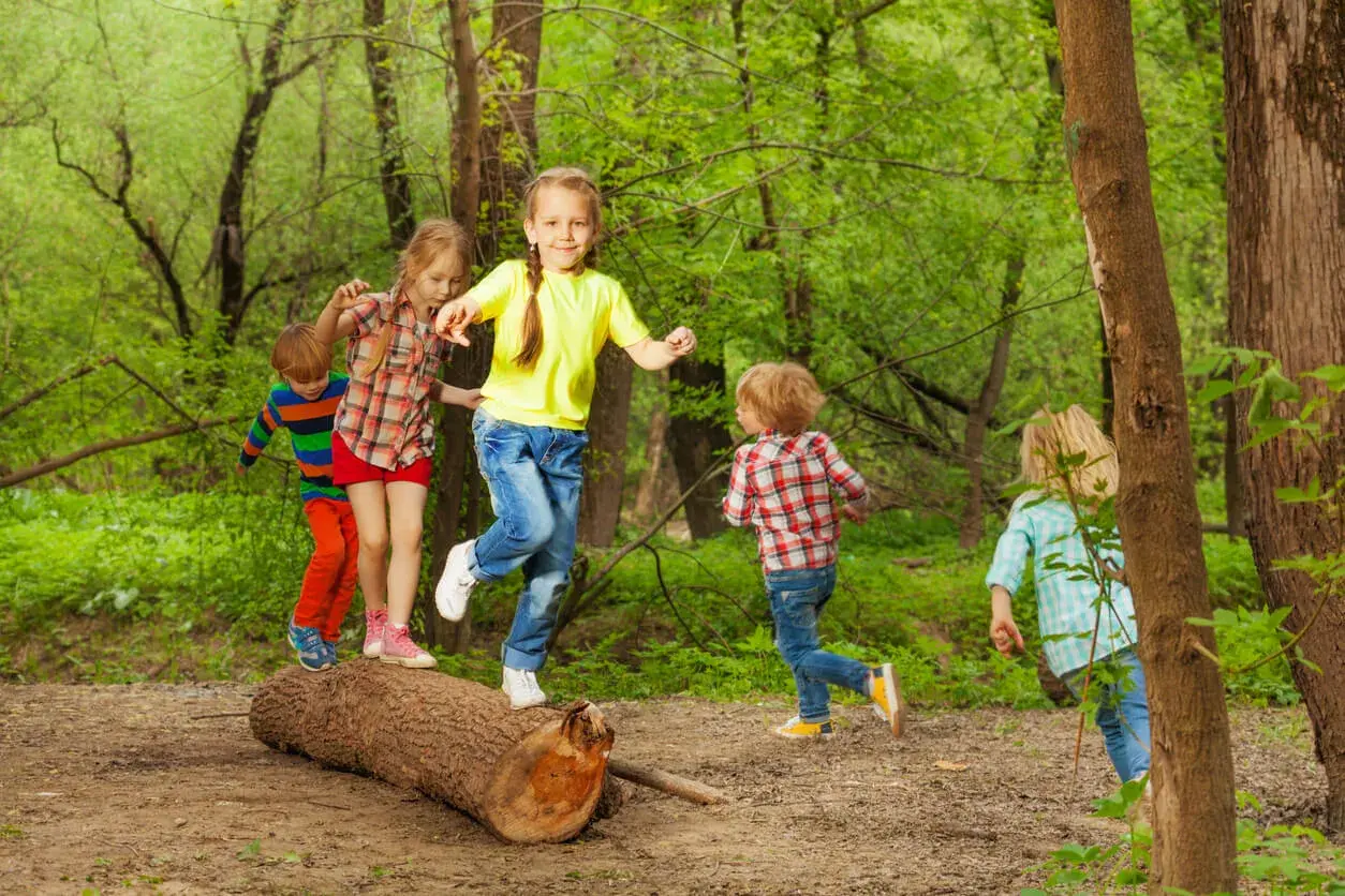 Niños jugando en un tronco, practicando el equilibrio. ¡Una escena de diversión y desarrollo para el equilibrio en niños de 1 a 2 años!