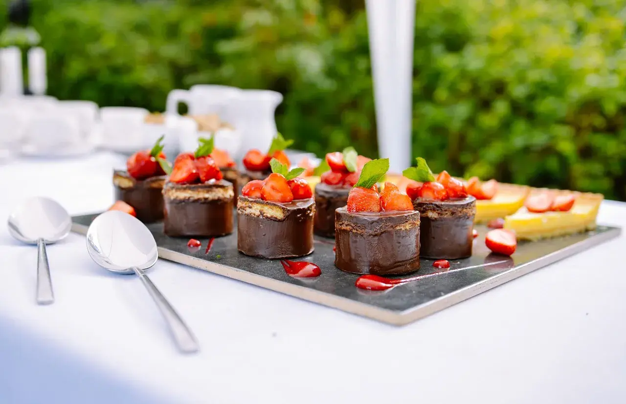 Catering przerwa kawowa: czekoladowe mini torty z truskawkami i cytrynowa tarta na eleganckim talerzu.