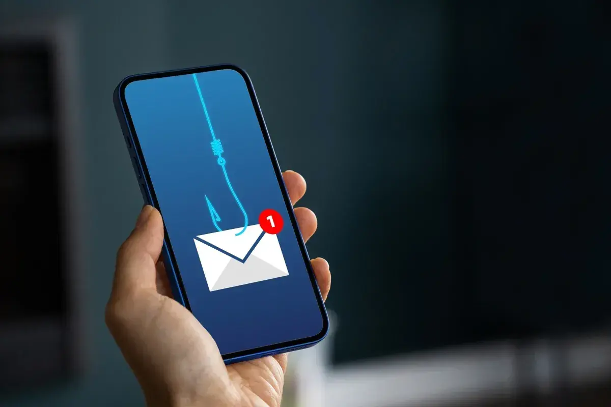 Telefon z ikoną koperty i haczykiem wędkarskim symbolizującym wyłudzenie pieniędzy. Uważaj na podejrzane wiadomości!