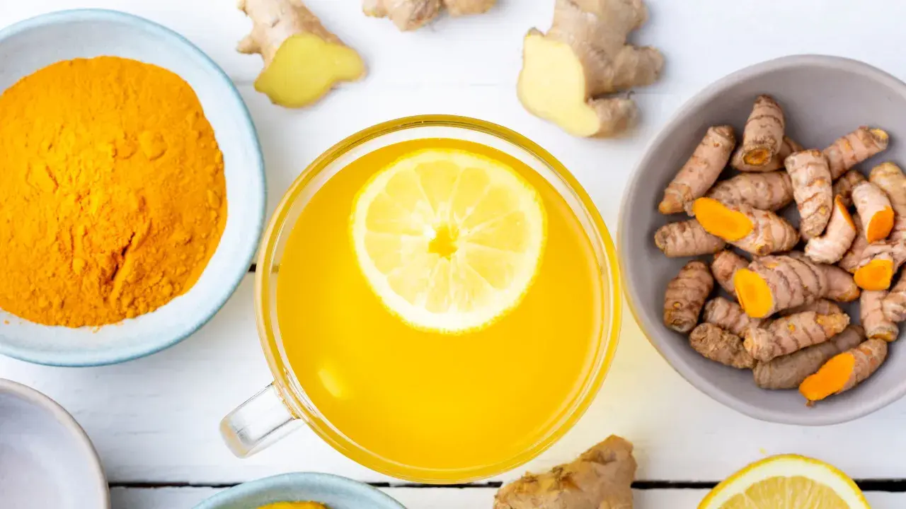 Tazza di bevanda gialla con limone, curcuma in polvere e radici, un potente antinfiammatorio naturale per intestino.