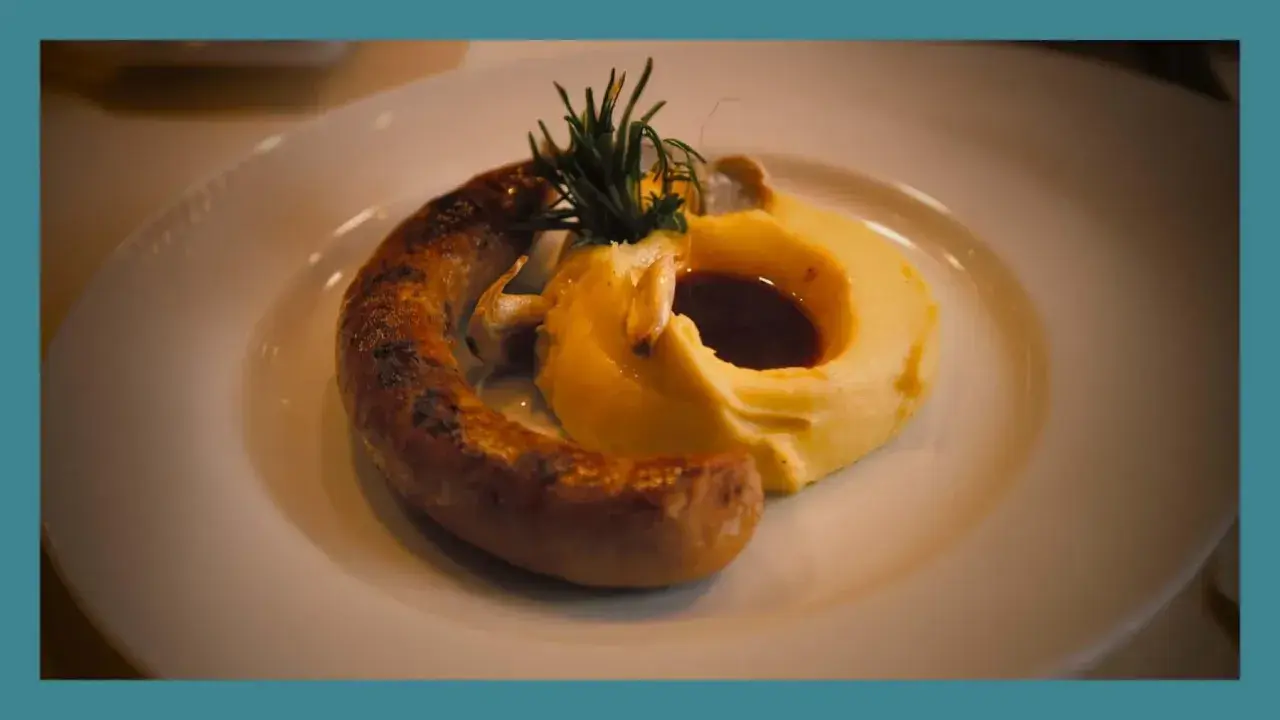 Une saucisse grillée, courbée sur une purée onctueuse, garnie de romarin et de sauce. Un plat réconfortant de saucisse purée.