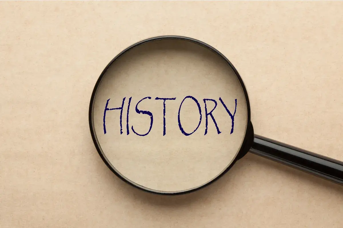 Lupa powiększająca napis "HISTORY" na papierze w kolorze beżowym.
