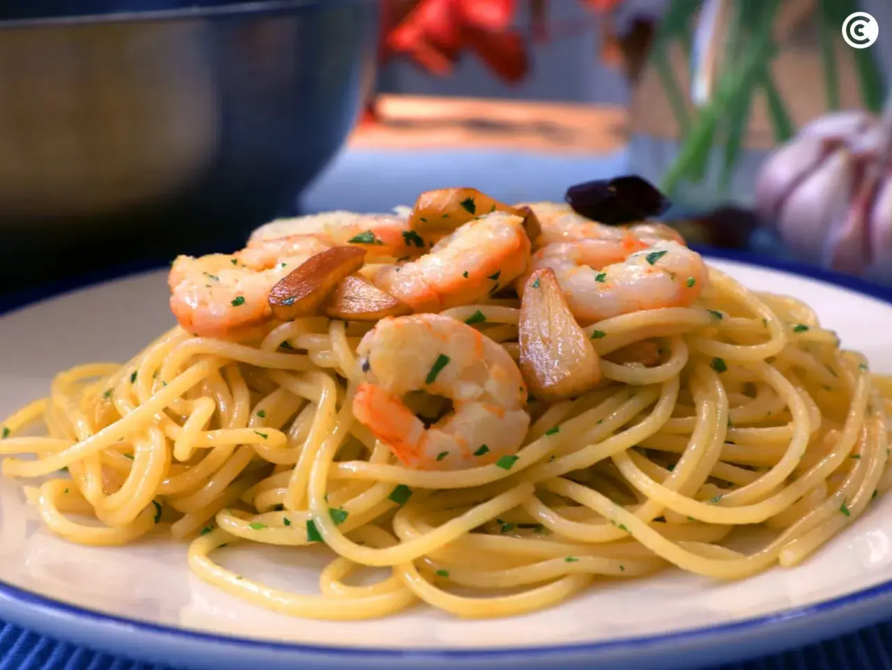 Espaguetis con gambas salteadas con ajo y perejil, servidos en un plato blanco con borde azul.