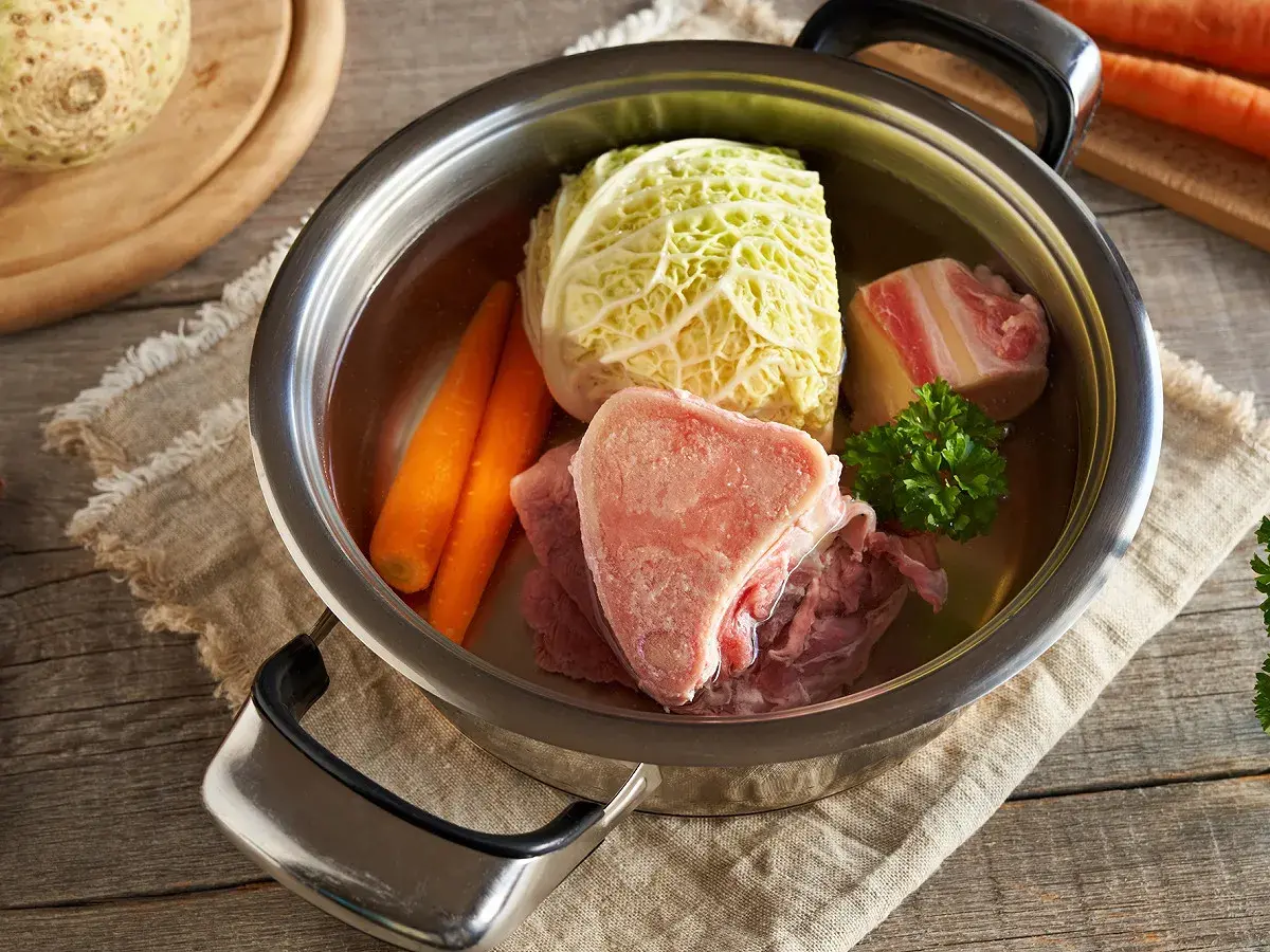 Une marmite de **potée au chou** avec des os de bœuf, des carottes, du chou et du persil, prête à mijoter.