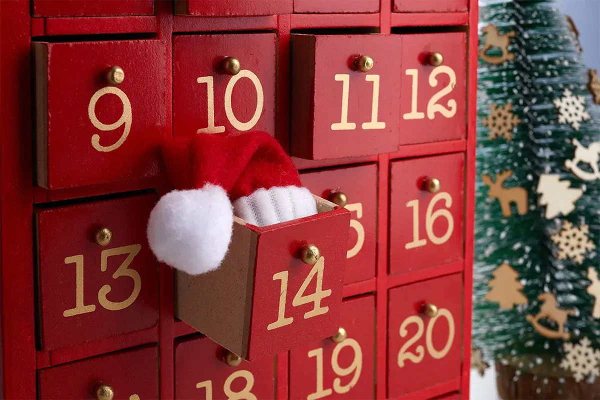 Un calendario dell'Avvento rosso con cassetti numerati. Il cassetto 11 è aperto, mostrando un cappellino di Babbo Natale. Ideale per idee su cosa mettere nel calendario avvento.