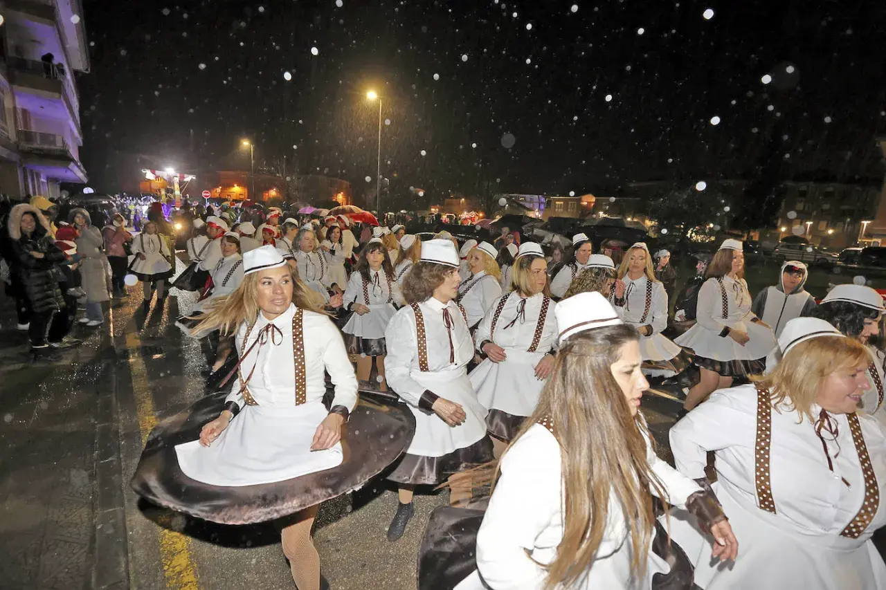 Desfile de mujeres con trajes blancos y sombreros en el carnaval cabezon de la sal, bajo una noche lluviosa.